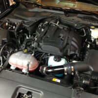 A car engine bay with various components visible, including the air intake, coolant reservoir, and engine cover.