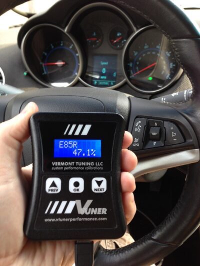 A hand holding a vehicle tuning device with a dashboard in the background.